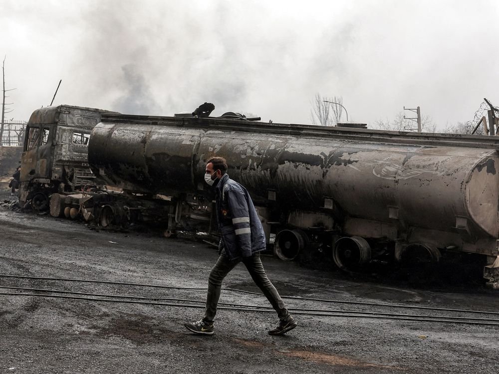 An Iranian civil defence member walks next to a destroyed fuel tanker vehicle near an ongoing fire following an overnight airstrike on the Shahran oil refinery in northwestern Tehran on March 8, 2026.